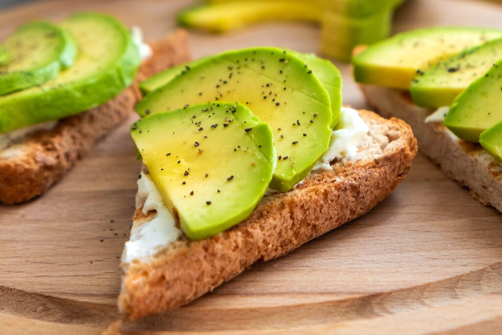 Tasty avocado sandwich with soft cheese, sliced avocado and pepper on toasted bread.
